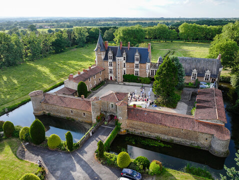 Aerial view of a stunning castle surrounded by a moat reflects in the water, its stone walls contrasting with the vibrant green landscape, Oree-d'Anjou, Pays de la Loire, France.