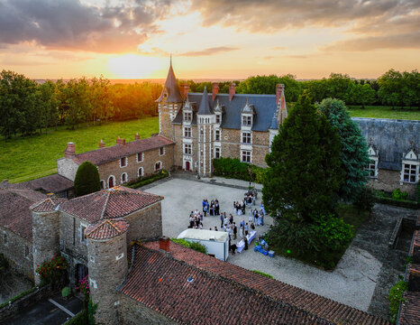 Aerial view of a medieval castle basking in the warm glow of the setting sun, its stone walls standing proudly against the lush green landscape, Oree-d'Anjou, Pays de la Loire, France.