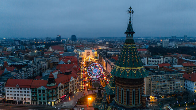 Aerial view of the illuminated Orthodox Cathedral and the Ferris wheel casting a warm glow over the city streets, Timisoara, Timis, Romania.