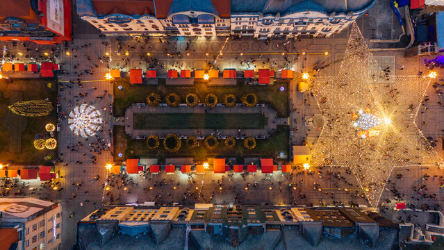 Aerial view of a bustling Christmas market in Victory Square, lights twinkling against the dark sky, casting a warm glow on the festive scene, Timisoara, Timis, Romania.
