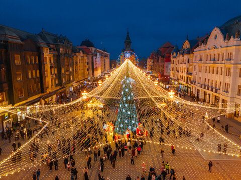 Aerial view of Union Square adorned with festive lights and a towering Christmas tree, casting a warm glow over the bustling crowd, Timisoara, Timis, Romania.
