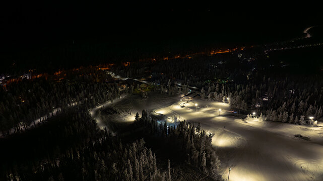 Aerial view of a snow-laden landscape, illuminated by the soft glow of lights scattered across the terrain, creating a serene and magical winter scene, Salla, Finland.