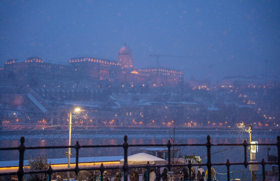 Budapest, Hungary - January 6, 2026: Buda Castle stands majestically on a hill overlooking the Danube River in Budapest, its grand facade illuminated against the heavy blue snowfall of a winter night.