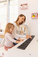 Little girl playing a piano with her mother