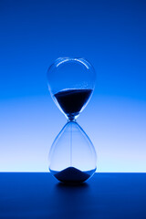 Hourglass with flowing sand symbolizing time passing, countdown, and deadline in blue light. Copy space