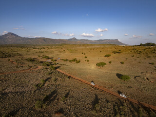 Aerial view of dirt roads cutting through the savannah, dotted with sparse green shrubs under a vast blue sky, Voi, Taita-Taveta County, Kenya.