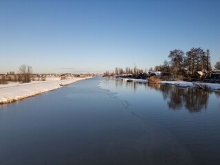 sun shines on icy river waterway after heavy snowfall in the Netherlands.  Drone footage of rural winter weather snow scene beautiful landscape  