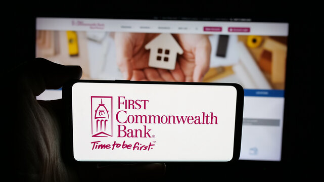 Stuttgart, Germany - 12-18-2025: Person holding cellphone with logo of US financial company First Commonwealth Bank on screen in front of webpage. Focus on phone display.