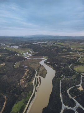 Aerial view of the meandering river snaking through the landscape towards the sea, its muddy waters contrasting with the dark green vegetation, Odeceixe, Faro District, Portugal.