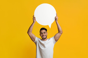 Excited attractive middle eastern millennial man showing blank speech bubble and smiling, sharing...