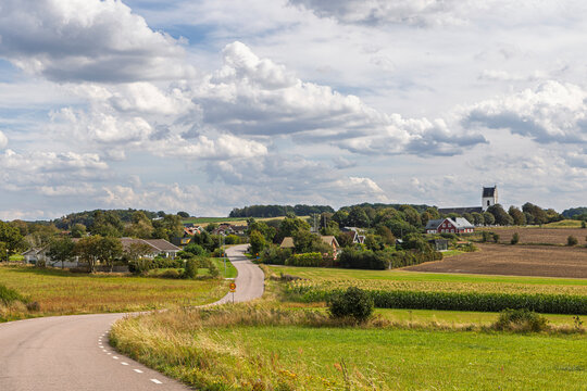 Tranquil Danish countryside village with winding road and distant church tower under a vast cloudy sky