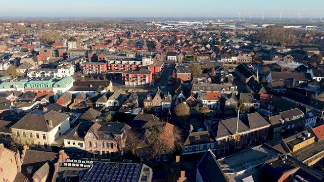 Aerial view of Dutch town red brick homes, solar rooftops, standout red white apartment block, and distant wind turbines reflect architectural diversity and sustainable planning.