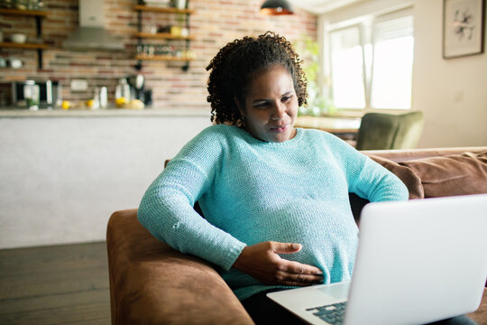 Adult pregnant woman focused on laptop at home