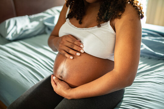 Adult woman tenderly cradling pregnant belly at home