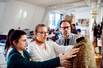 Adult coworkers reviewing sweater with focused expressions in fashion studio