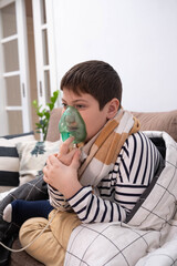 Boy wrapped in blanket using inhaler mask, sitting on sofa at home, recovering from illness, glass of water nearby, cozy indoor setting.