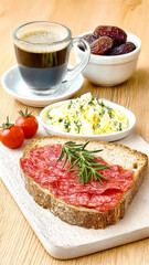 Salami open sandwich with a side of creamy herb eggs and dried dates.