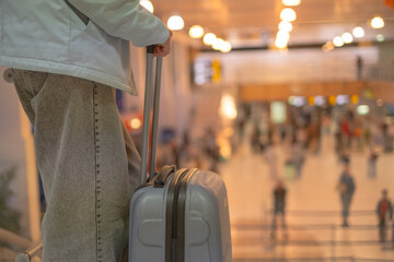 Travelers move through busy airport terminal as a person waits by luggage near the entrance on a sunny afternoon