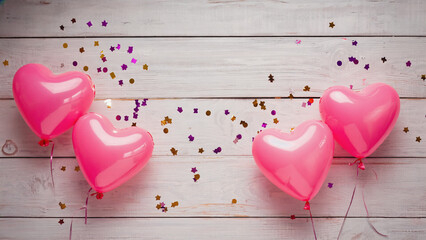 Pink heart balloons with confetti on wooden background  