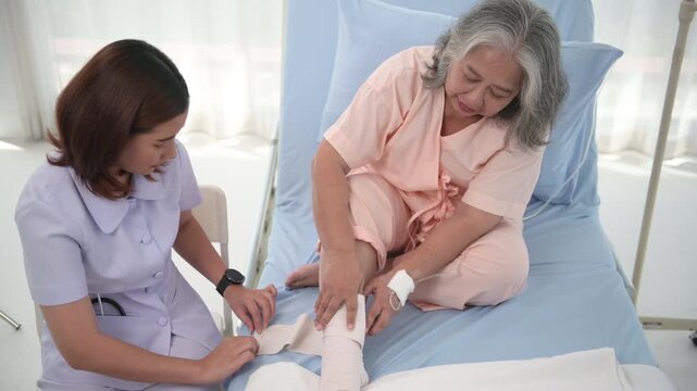 Asian female nurse bandaging foot of elderly woman patient at the hospital.