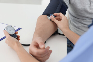Nurse checking man's blood pressure with sphygmomanometer at table in hospital, closeup