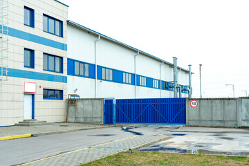 The facade of an industrial building or warehouse with large windows. Modern factory buildings or warehouses. Large metal gates and a concrete fence.