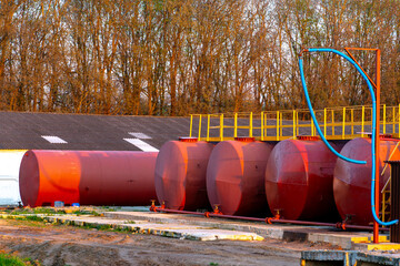 Large metal tanks for storing gasoline, gas or oil. Red barrels on the territory of the enterprise under the open sky during sunset.