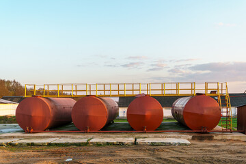 Large metal tanks for storing gasoline, gas or oil. Red barrels on the territory of the enterprise under the open sky during sunset.