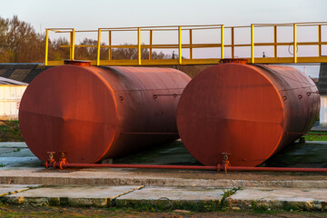 Large metal tanks for storing gasoline, gas or oil. Red barrels on the territory of the enterprise under the open sky during sunset.