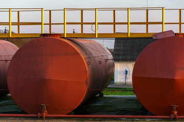 Large metal tanks for storing gasoline, gas or oil. Red barrels on the territory of the enterprise under the open sky during sunset.