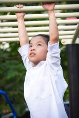 Obraz premium Action portrait of a young girl hanging from monkey bars at a playground, showing effort and concentration. Highlighting physical development, outdoor exercise, and the resilience of active childhood.