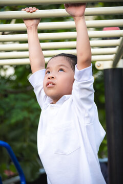 Action portrait of a young girl hanging from monkey bars at a playground, showing effort and concentration. Highlighting physical development, outdoor exercise, and the resilience of active childhood.