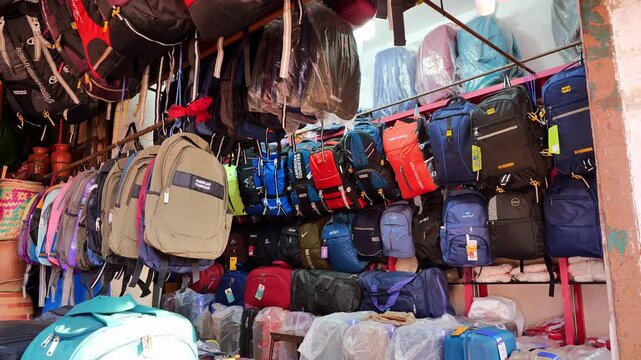 variety of colorful backpacks hanging and stacked in crowded outdoor market shop with vibrant travel gear display
