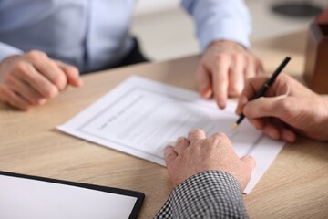 Notary showing senior man where to sign Last Will and Testament at wooden desk in office, closeup