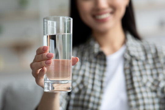 Glass of fresh spring water in young woman hand, closeup. Unrecognizable lady recommending water drinking, showing glass full of water. Healthy lifestyle, hydration concept