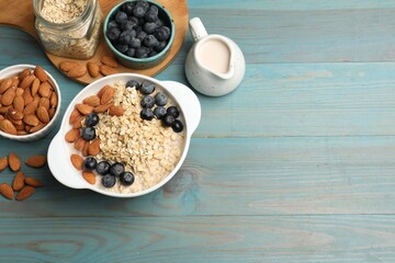 Tasty oatmeal with almond milk, nuts and blueberries on light blue wooden table, flat lay. Space...