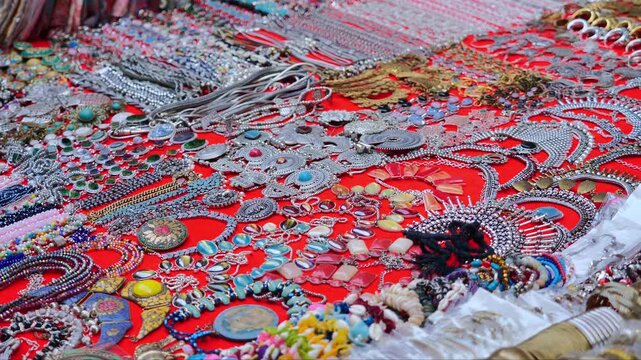 assorted colorful jewelry pieces displayed on red market cloth with vibrant beads stones and metal ornaments
