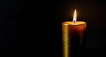 Gold candle burns with warm flame against dark background and copyspace