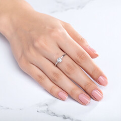Naklejka premium Elegant closeup of a womans manicured hand wearing a stunning silver solitaire diamond engagement ring on a marble surface. Perfect for wedding, jewelry, and luxury lifestyle branding.