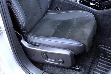 Close up leather driver seat. Modern car interior with a black combined leather and Alcantara sport seat. Features electric seat adjustment controls and detailed white contrast stitching on the driver