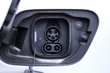 Close-up of an electric vehicle's charging port on a white car body. Black plastic charging connector with rubber seal, AC contacts, DC quick-release connector, automotive technology, energy supply.