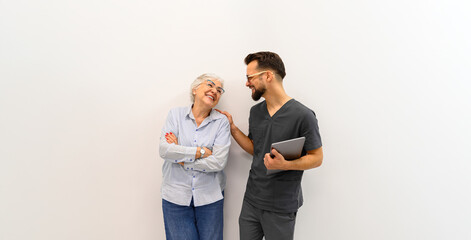 Happy male ophthalmologist with laptop talking with senior patient while standing against white background