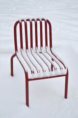 Red metal chair standing isolated on the snow background. Closeup outdoors photo.  Snow covered chair in winter yard.