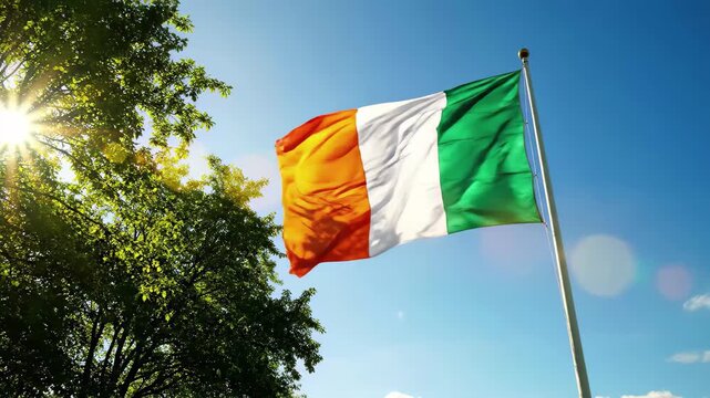 Flag of cte divoire waving in the bright sun against a clear blue sky with green tree leaves on the left side