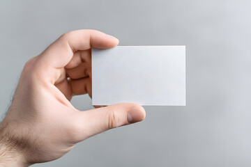 Obraz premium Hand holds a blank card in front of a plain gray background in a simple setting