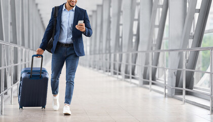Unrecognizable Young Businessman Using Smartphone While Walking With Suitcase In Airport, Smiling...