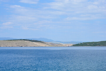 A scenic view from Jadranovo captures the Krk Bridge spanning the blue sea, connecting the mainland to Krk Island under a partly cloudy sky