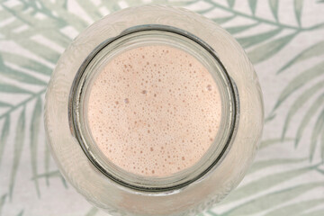 A top down bird eye view of a glass bottle neck filled with creamy frothy hazelnut milk showing small bubbles on the surface