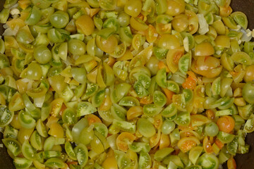 A top down shot of numerous small green and yellow cherry tomatoes chopped into quarters and halves being sauteed in a frying pan