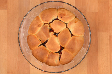 A top down view of freshly baked pull apart sweet buns with jam filling on a glass plate over a wooden surface